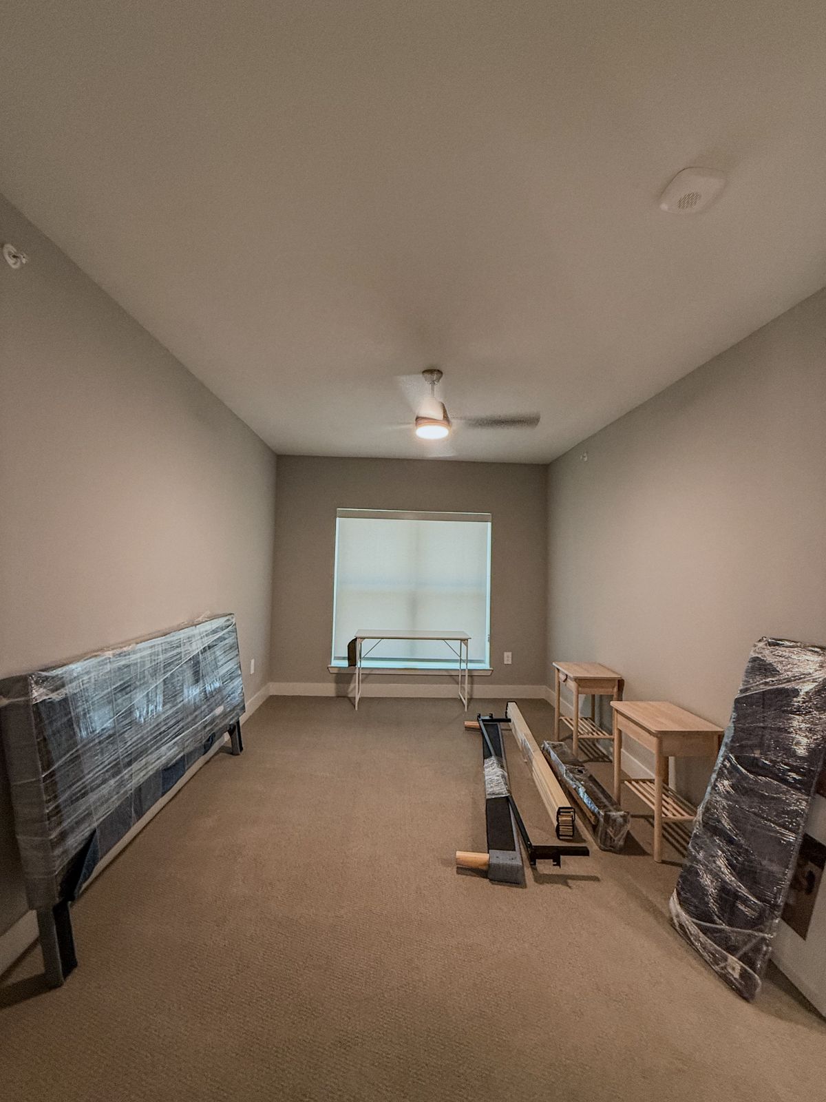 Wrapped headboard pieces, bed rails, nightstands, and assembly equipment are staged in a carpeted bedroom.