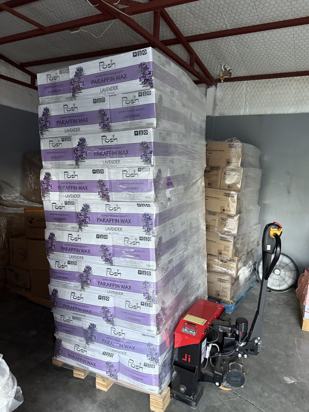 Cases of commercial products are stacked, stretch-wrapped, and secured on pallets beside powered moving equipment.