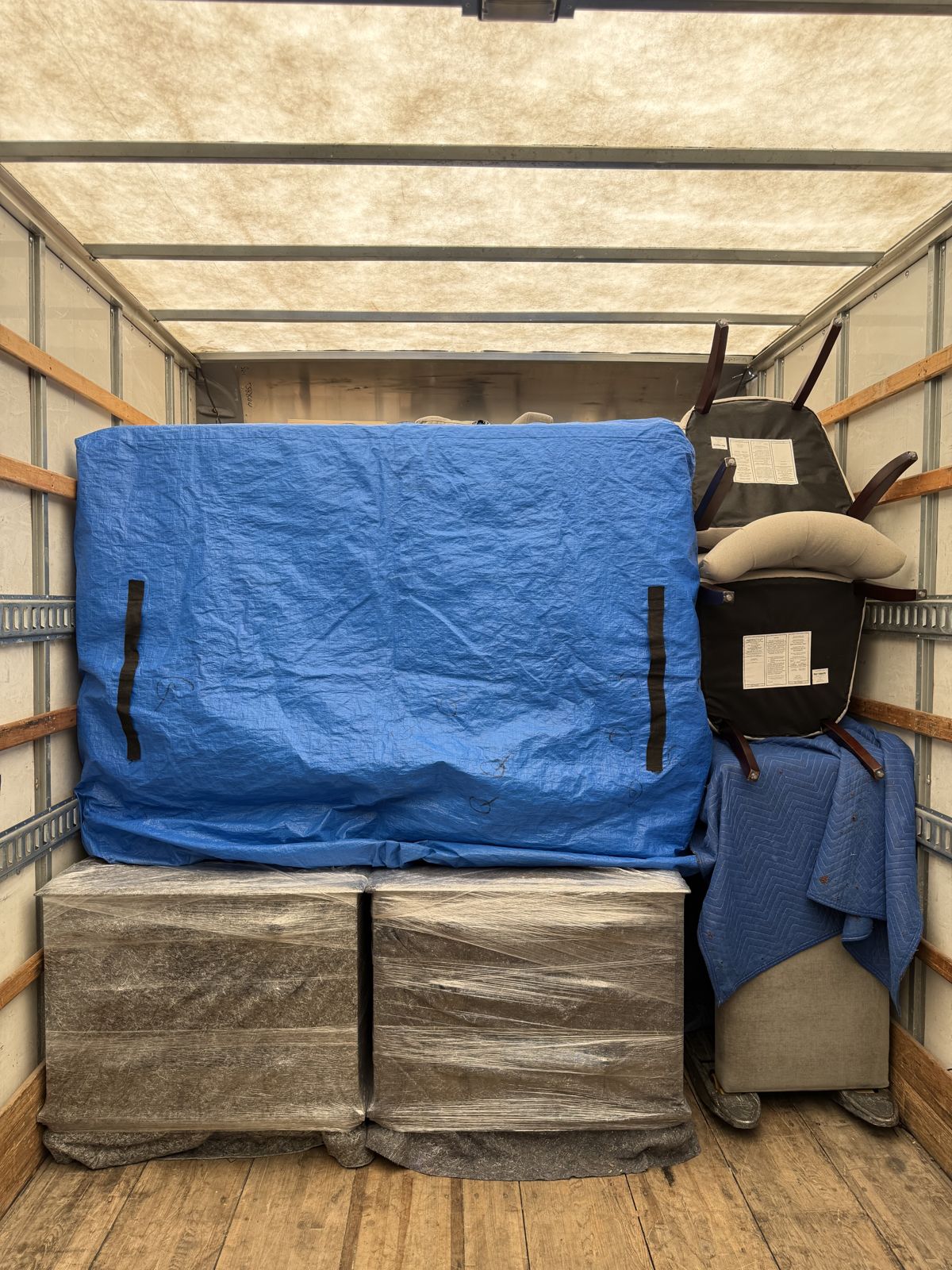 Blanket-wrapped furniture and chairs are tightly arranged inside a TL Moving truck.