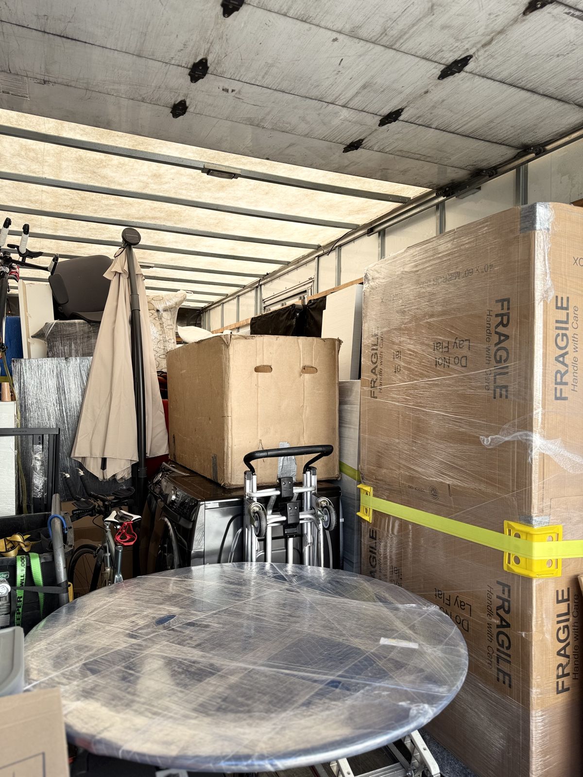 Wrapped furniture, boxes, a hand truck, and other moving equipment fill the interior of a box truck.
