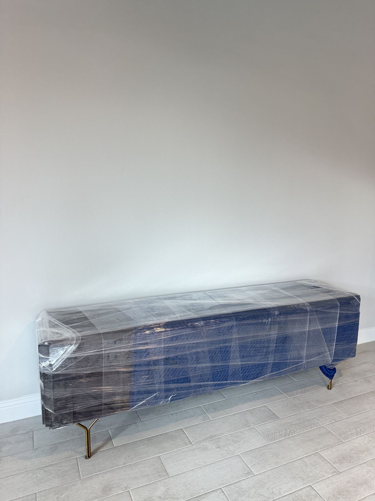 A long upholstered bench is fully protected with clear stretch wrap before transport.