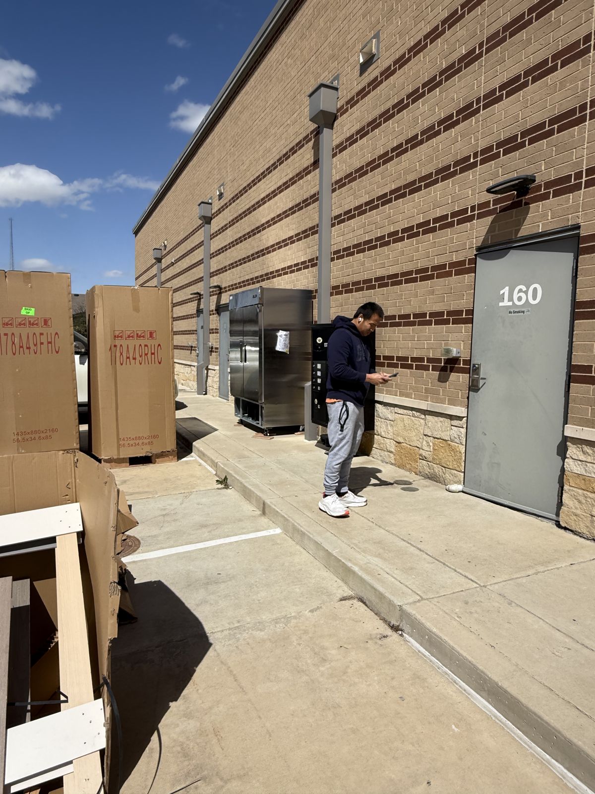 A TL Moving crew member stands near boxed and stainless-steel commercial equipment outside a building.