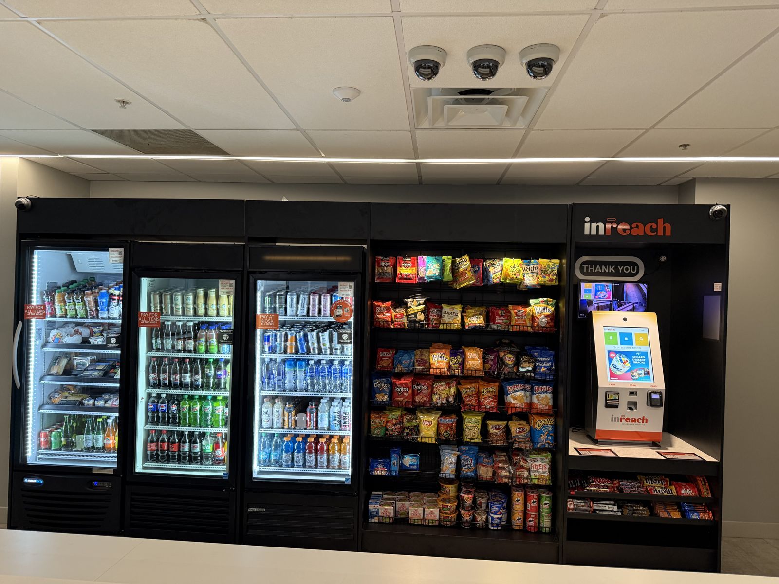 A completed self-service micro market includes refrigerated cases, snack shelving, and a payment kiosk.