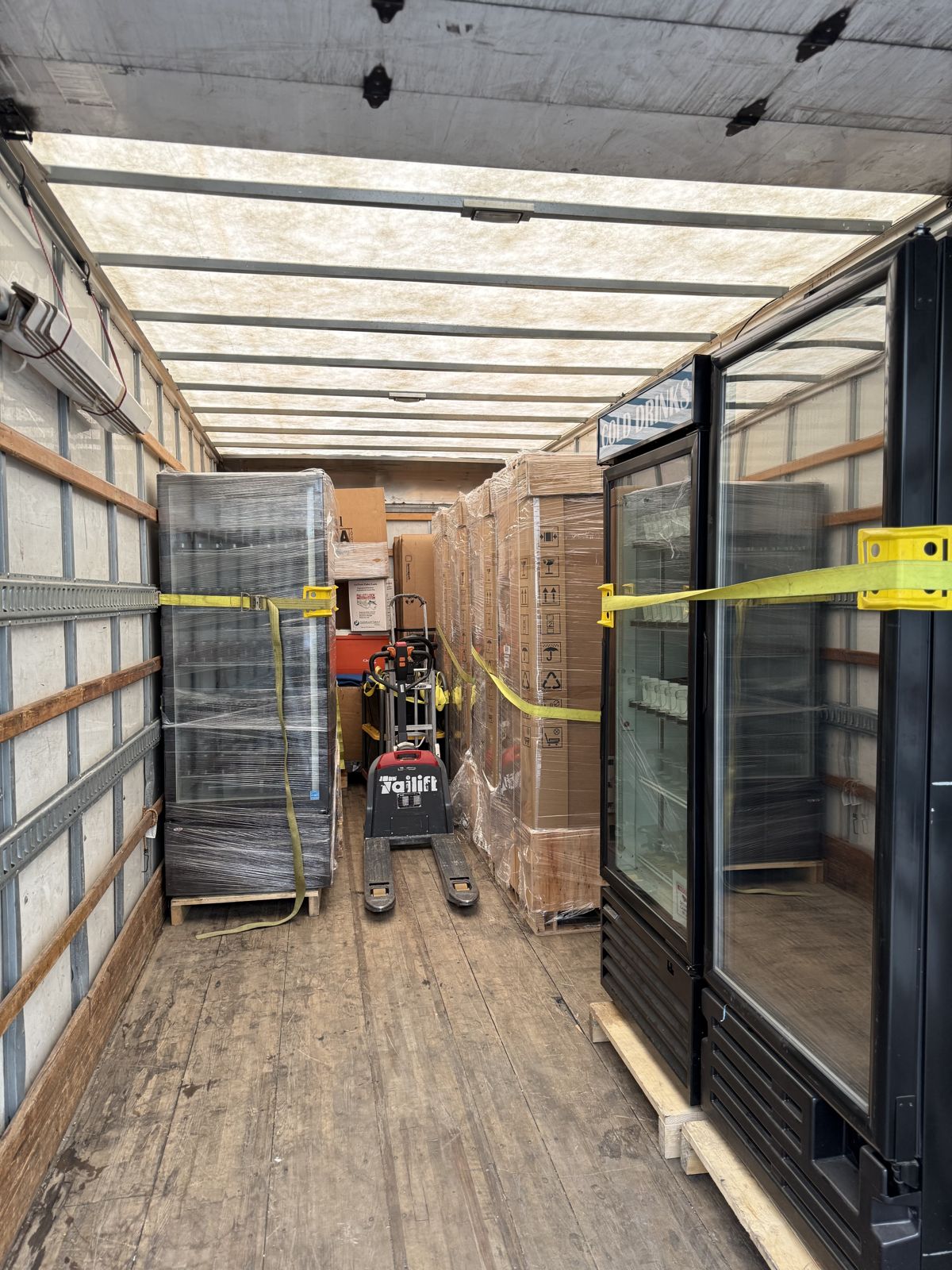 Commercial coolers, wrapped pallets, and a pallet jack are secured inside a moving truck.