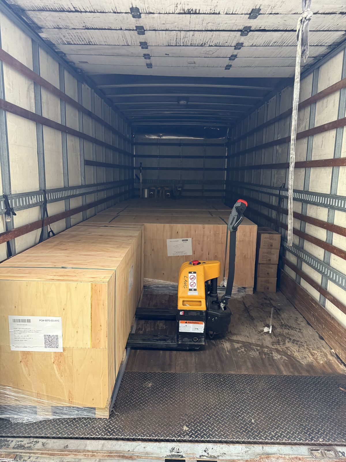 Large wooden shipping crates and a powered pallet jack sit inside a TL Moving truck.