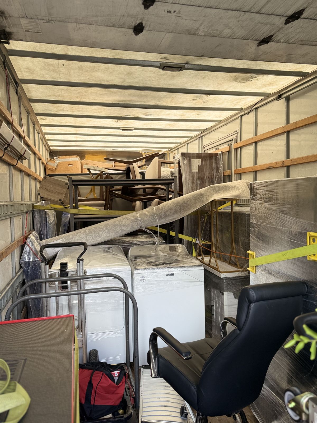 A moving truck is densely loaded with wrapped appliances, office furniture, chairs, and secured specialty items.
