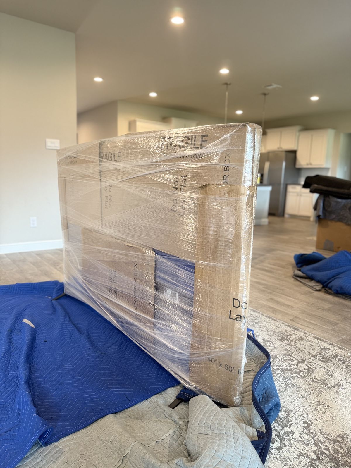 A mirror carton is fully secured with protective padding and clear stretch wrap beside moving blankets.