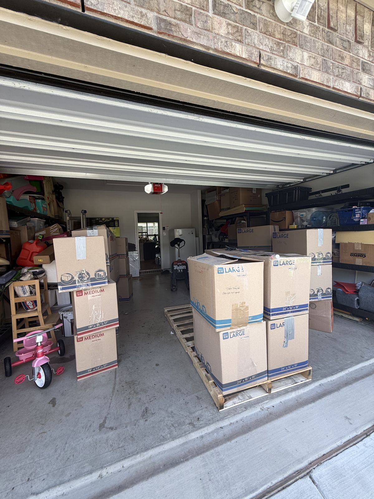 Sealed moving boxes are stacked on pallets and throughout an open residential garage.