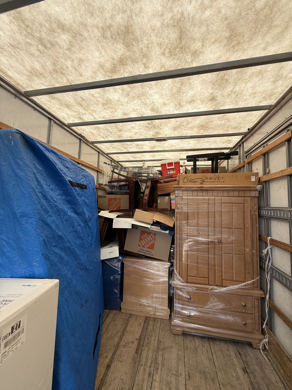 Wrapped household furniture, boxes, and moving blankets are packed inside a moving truck.