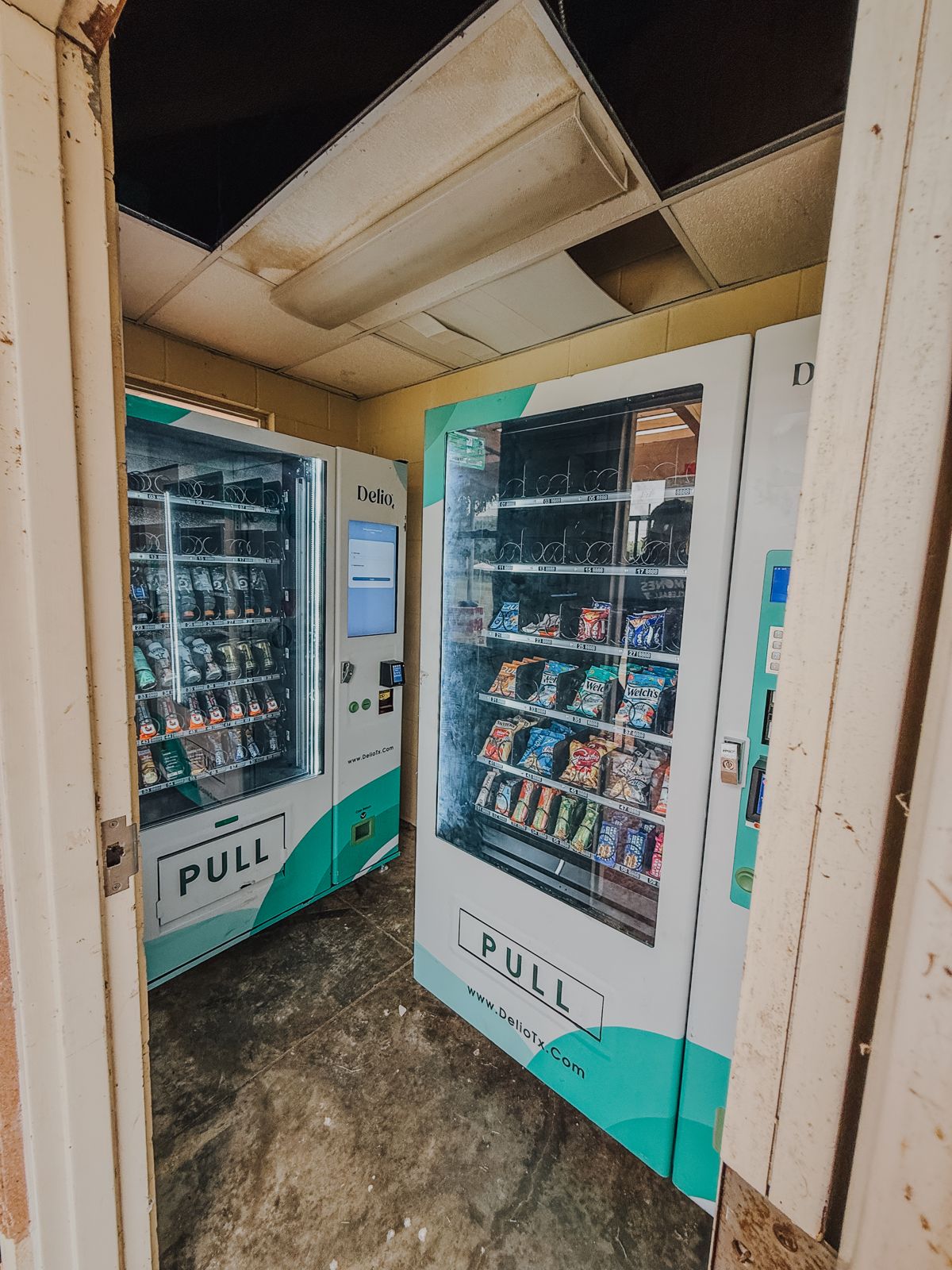 Two glass-front snack vending machines stand inside a small commercial room.
