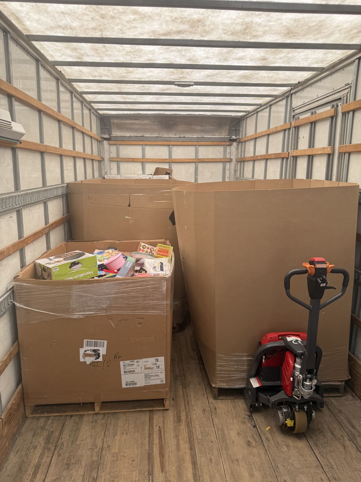 Large cardboard shipping cartons and a smaller packed container sit on pallets inside a moving truck.