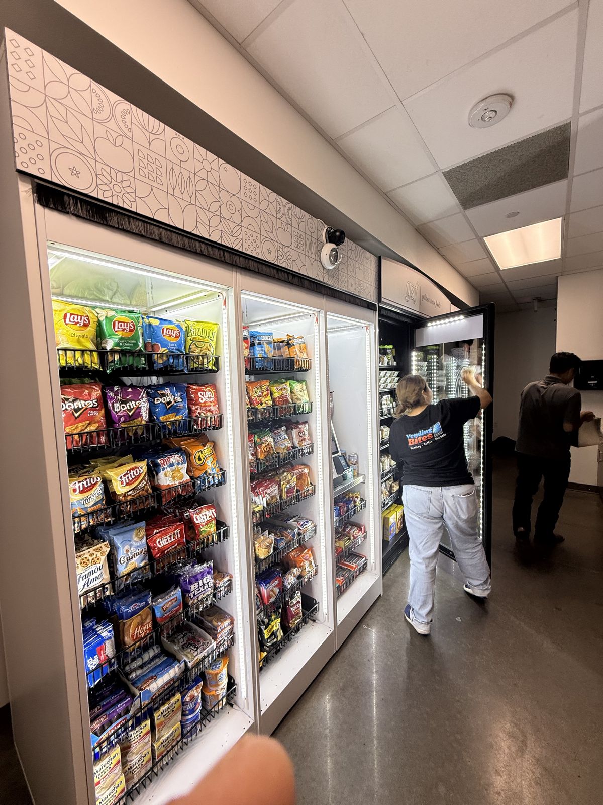 Workers stock and service illuminated snack and beverage vending units during a commercial installation.