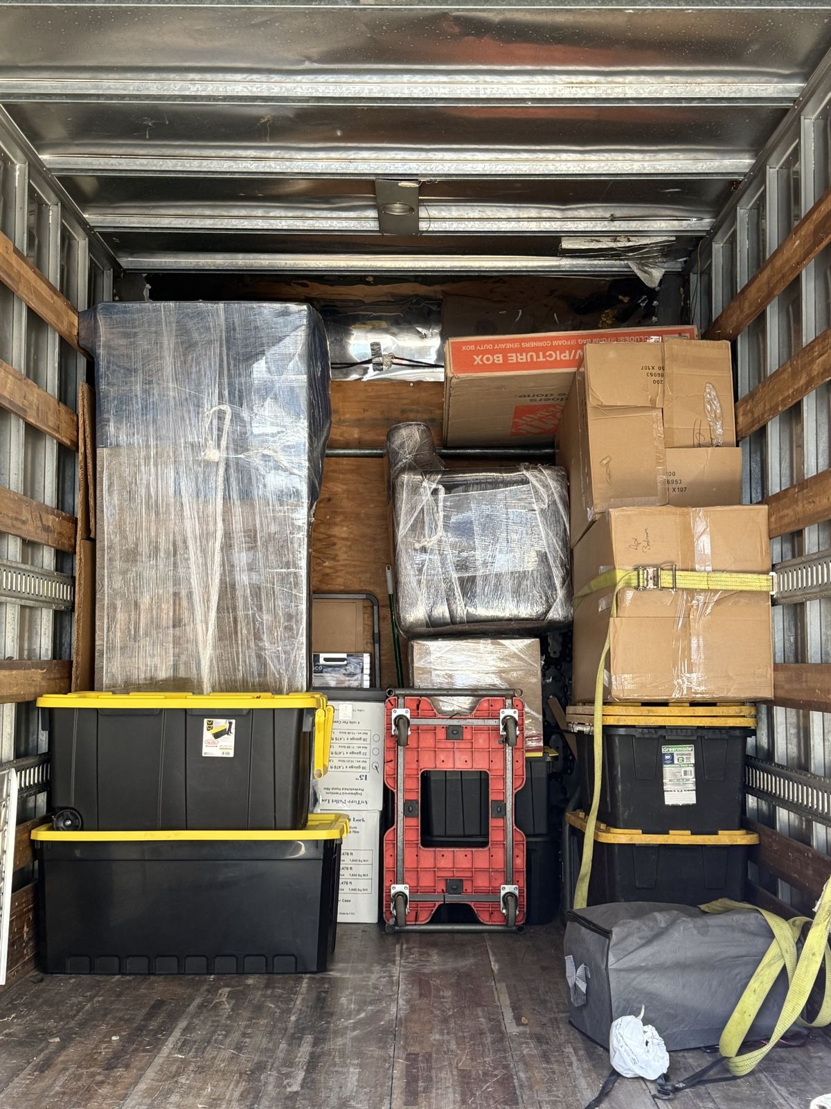 Wrapped furniture, cardboard boxes, storage totes, and moving equipment fill a moving truck.