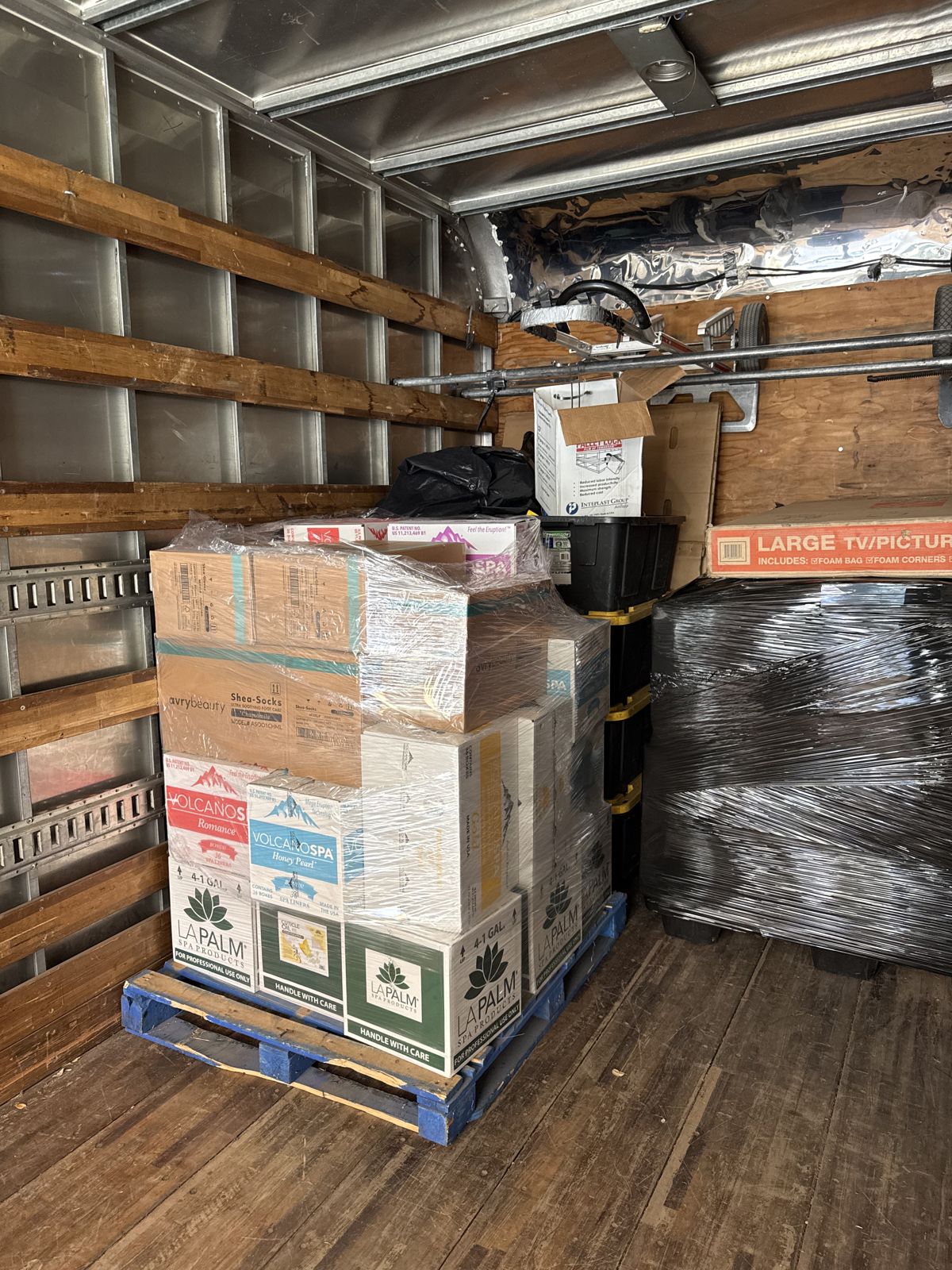 Stacked boxes on a pallet and a large wrapped item are organized inside a moving truck.