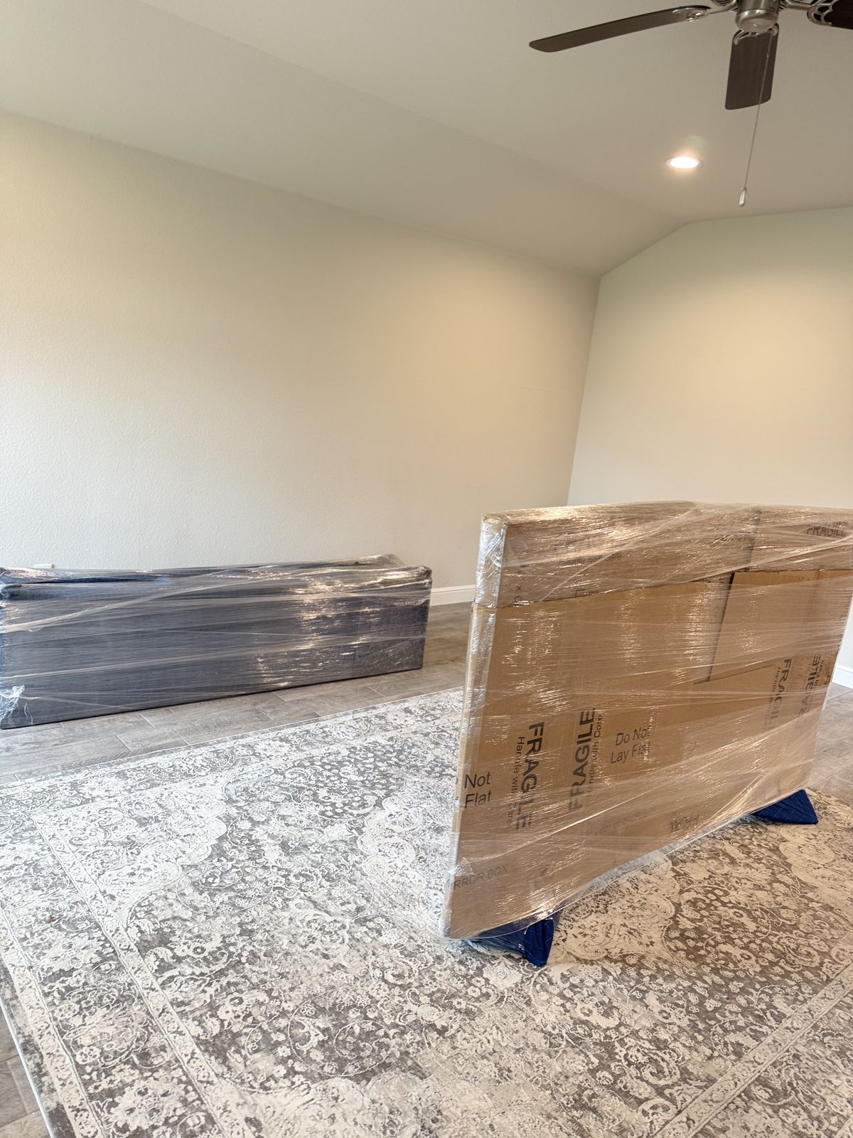 Blanket-wrapped and boxed furniture rests on protective floor pads inside a bright residential room.