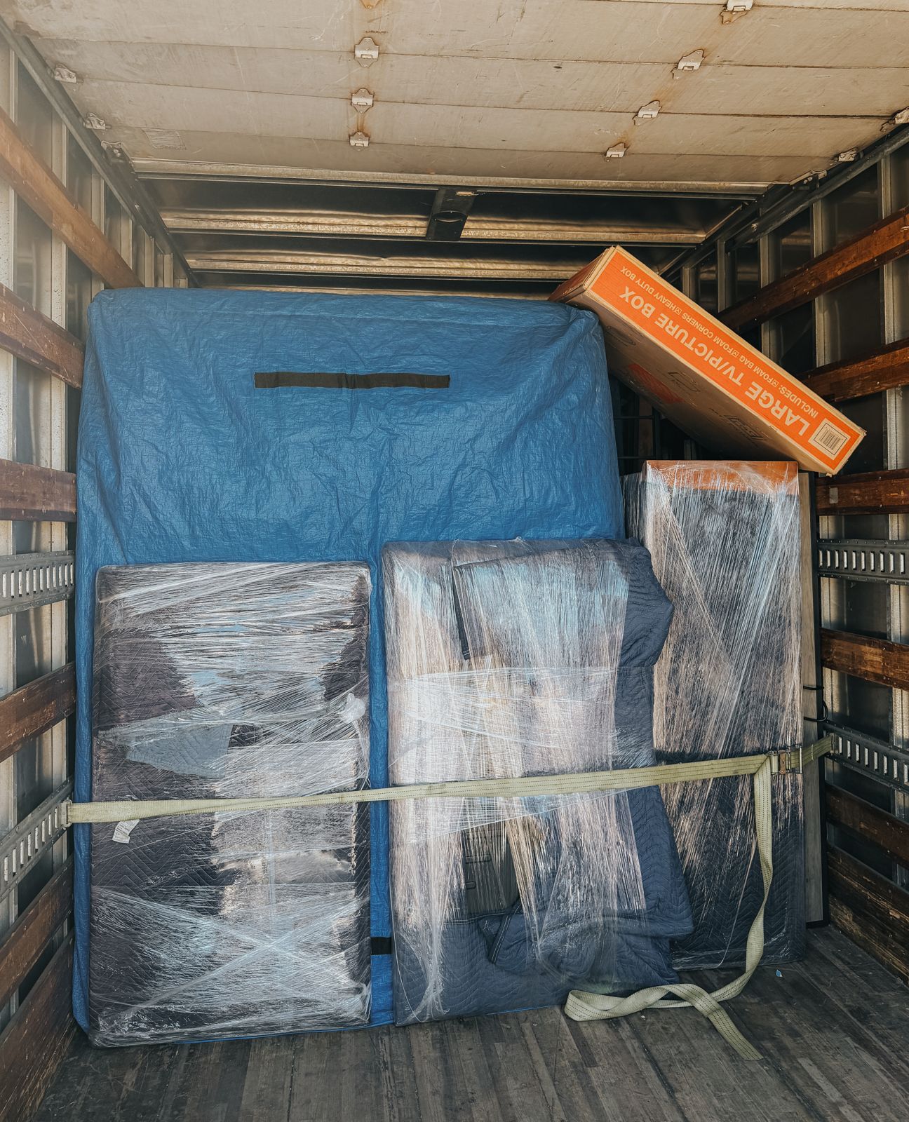 Wrapped furniture and a blue moving blanket are secured with straps inside a TL Moving truck.