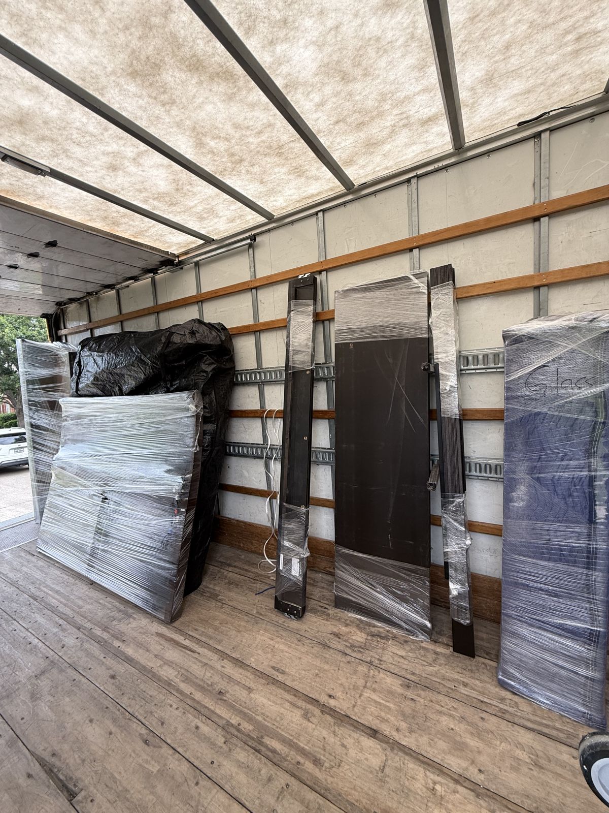 Wrapped furniture panels and other protected household pieces stand along the wall of a moving truck.