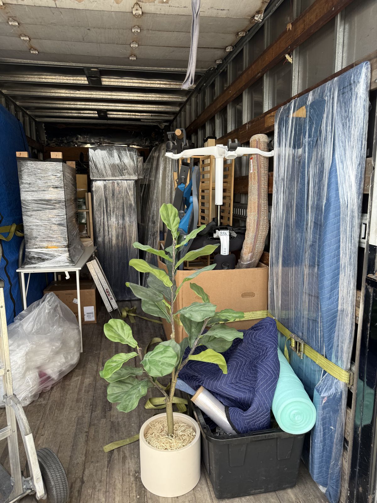 Wrapped furniture, moving blankets, bins, and a potted plant are secured inside a moving truck.