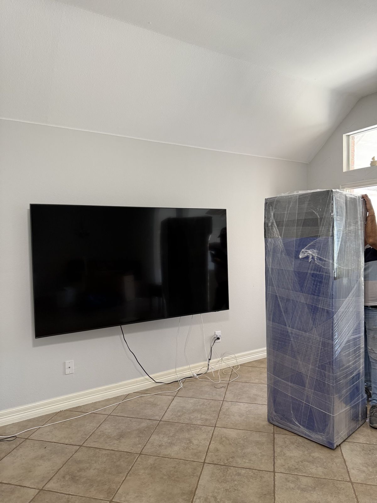 A tall household item is fully wrapped for protection beside a wall-mounted television.