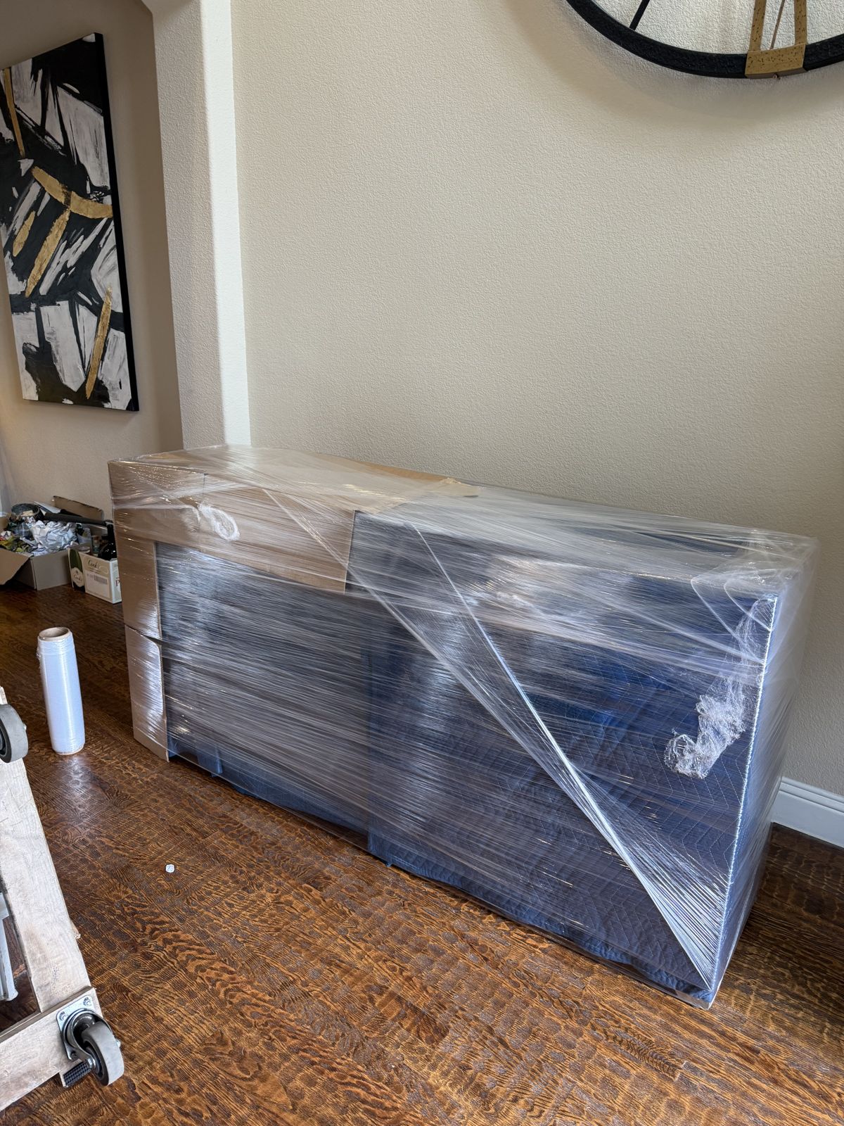 A large wooden cabinet is carefully covered in stretch wrap inside a furnished residence.