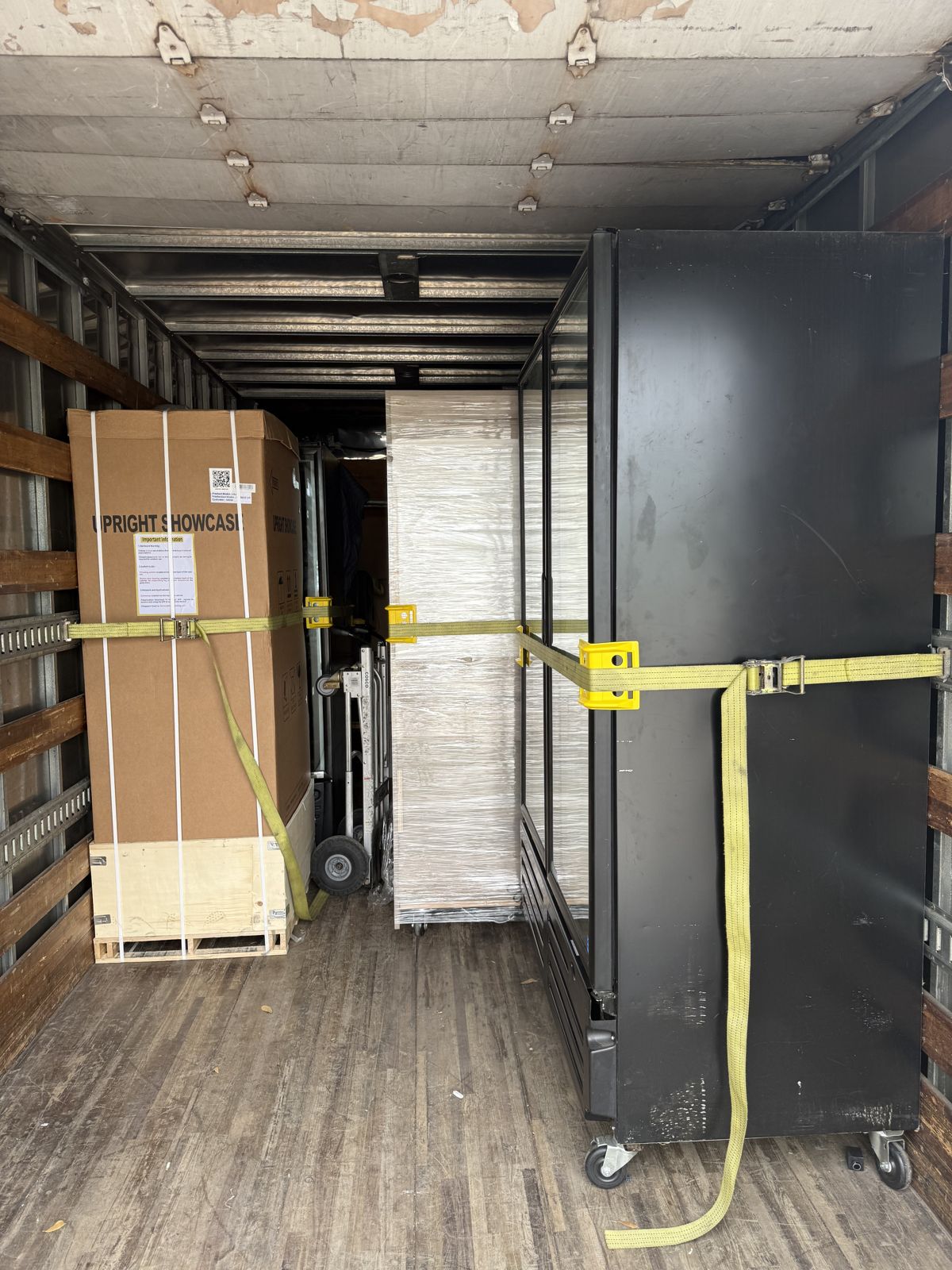 Large commercial cabinets and wrapped equipment are secured with yellow straps inside a TL Moving truck.