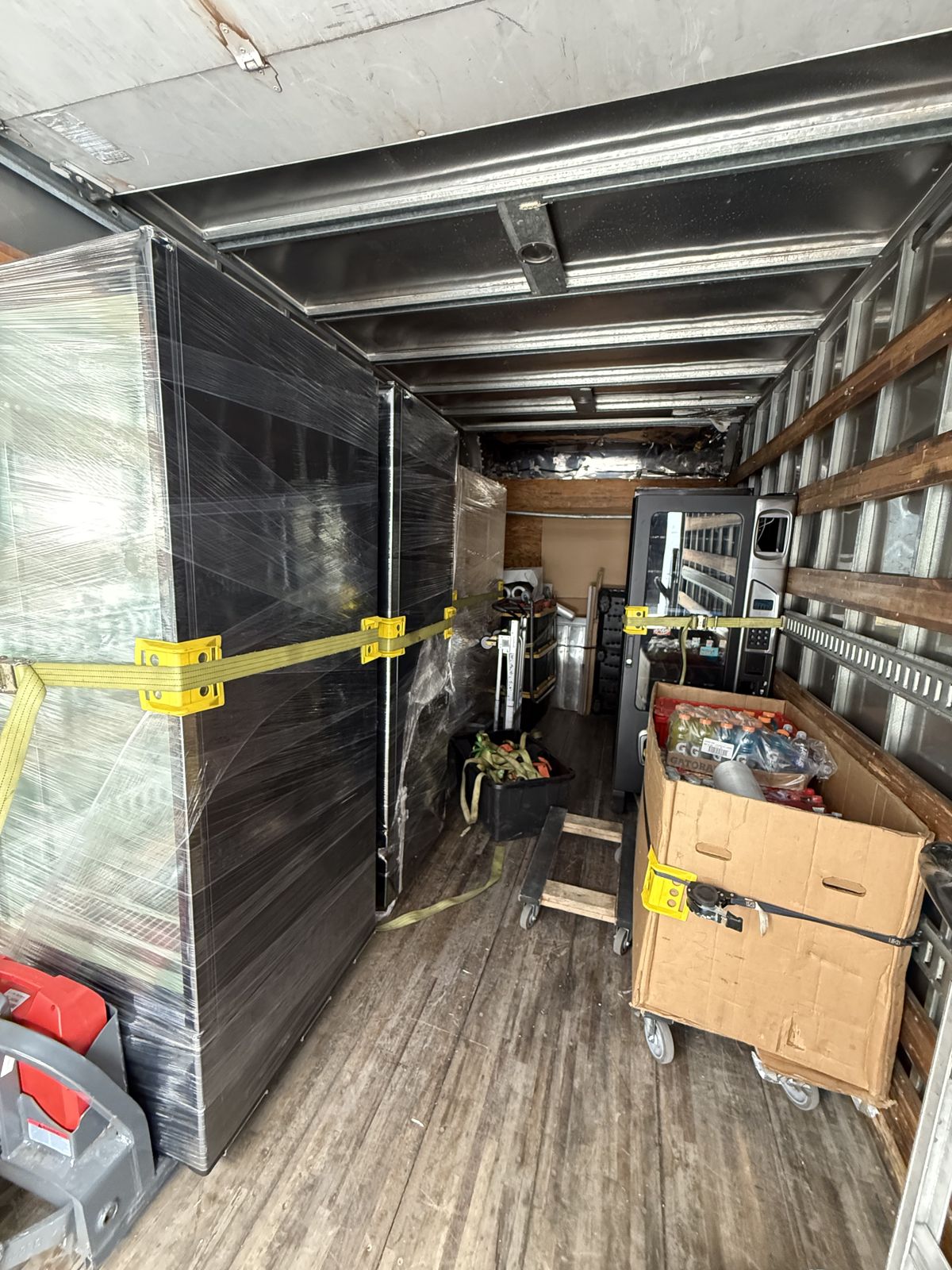 TL Moving equipment secures wrapped vending machines and a rolling supply cart inside a box truck.
