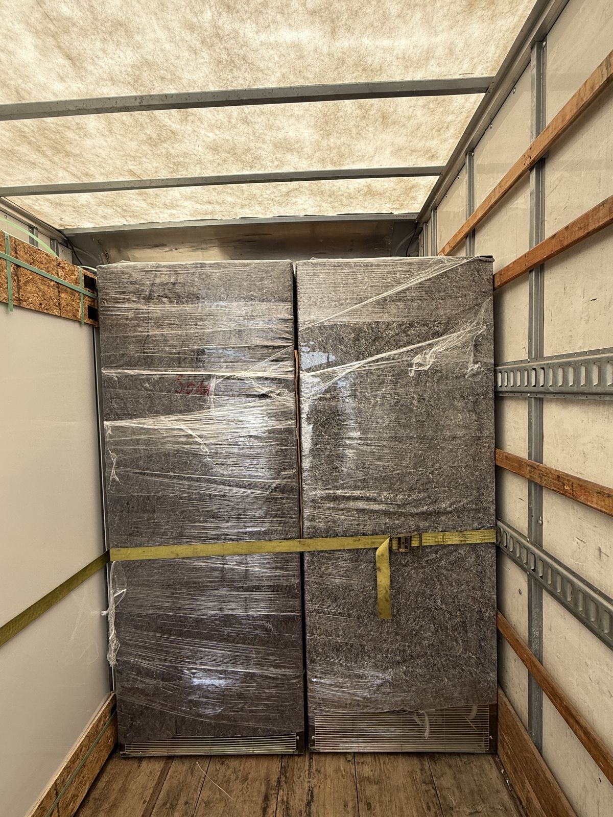 Four large wrapped units are tightly strapped inside a moving truck.