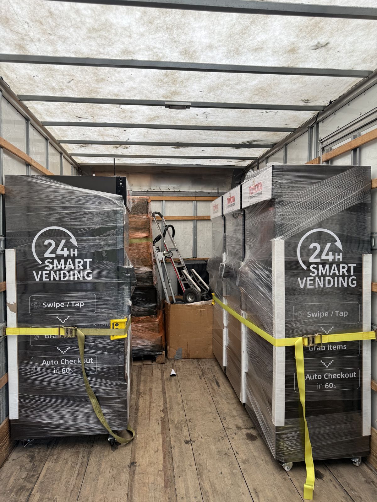 TL Moving equipment secures two wrapped smart vending units with yellow straps inside a box truck.