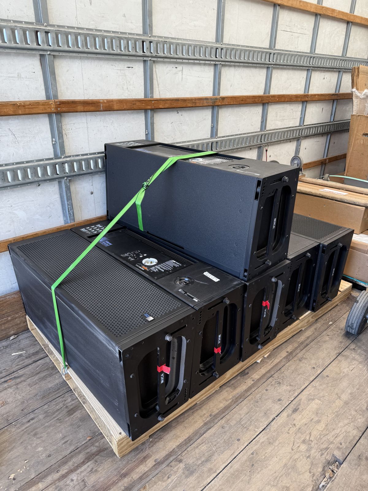 Several large black commercial equipment units are stacked on a pallet and secured with a green strap.