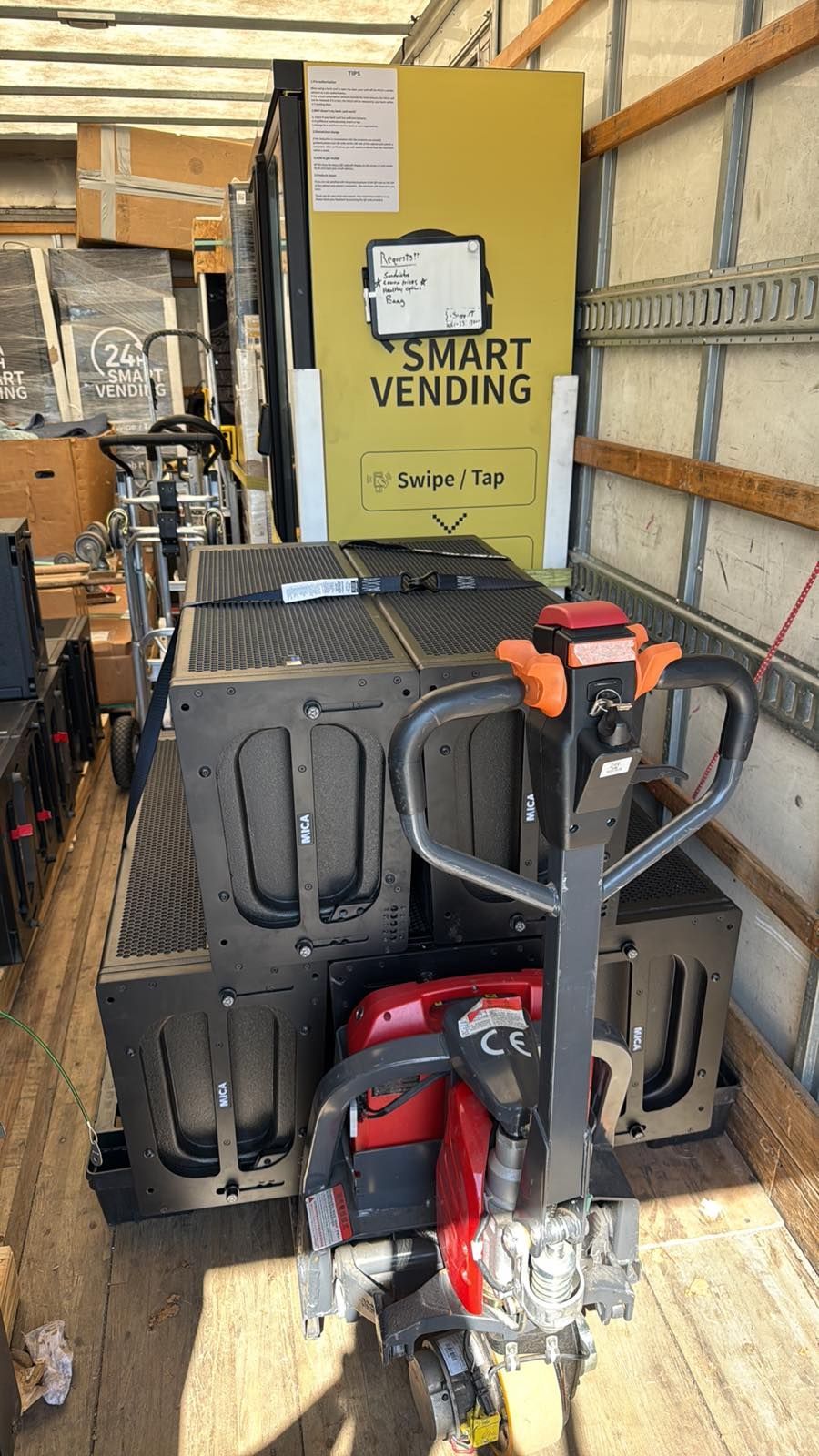 A smart vending unit and stacked equipment are loaded inside a truck with a powered pallet jack.