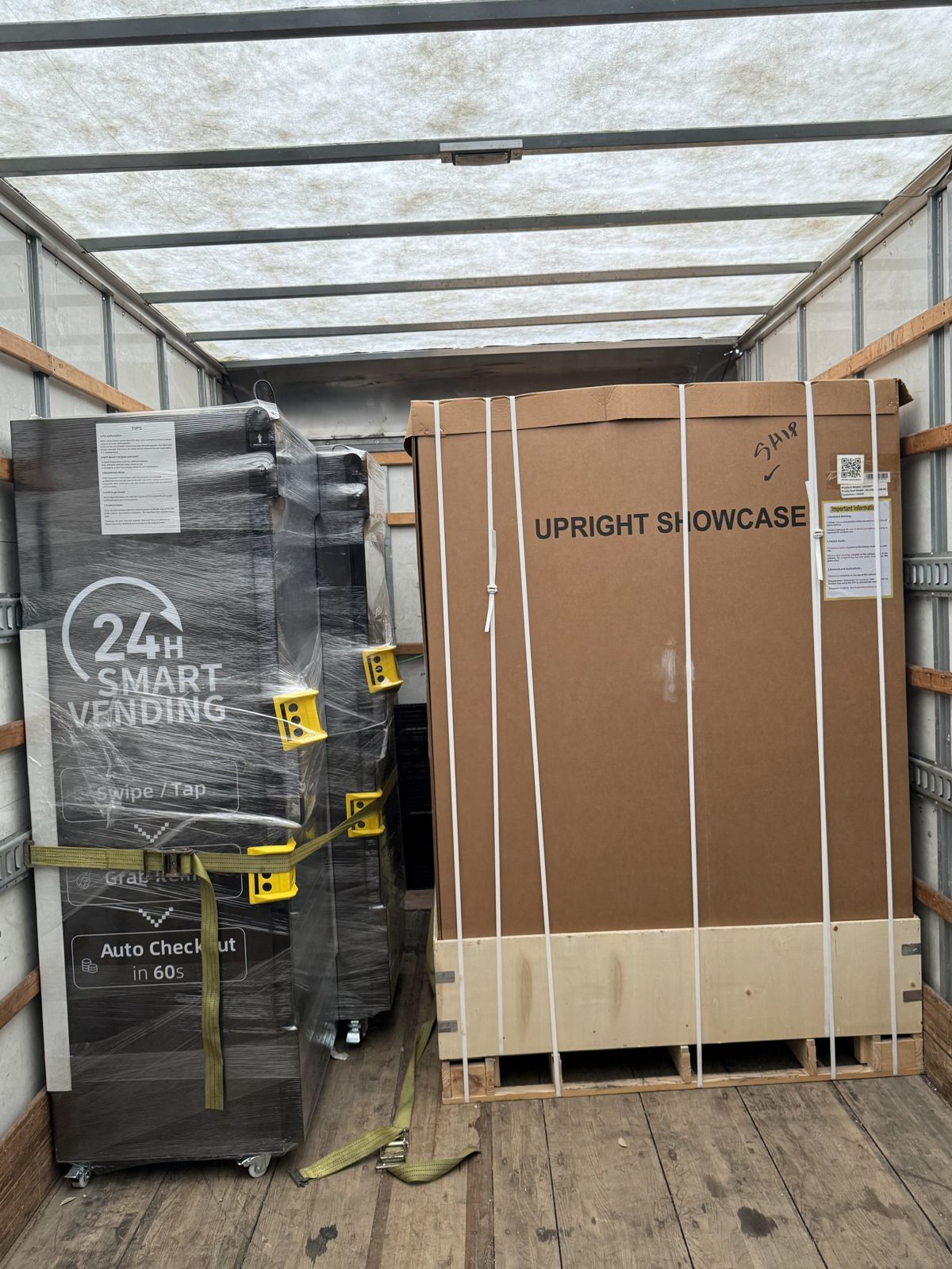 A wrapped smart vending machine and a crated upright showcase are secured inside a moving truck.