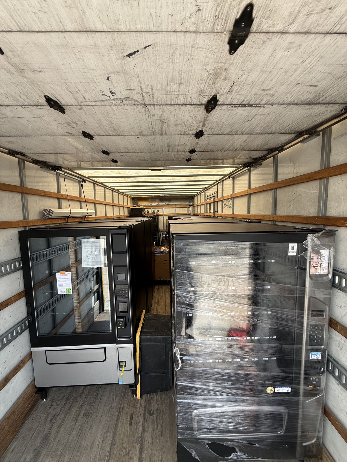 Two vending machines, including one wrapped for protection, are positioned inside a moving truck.