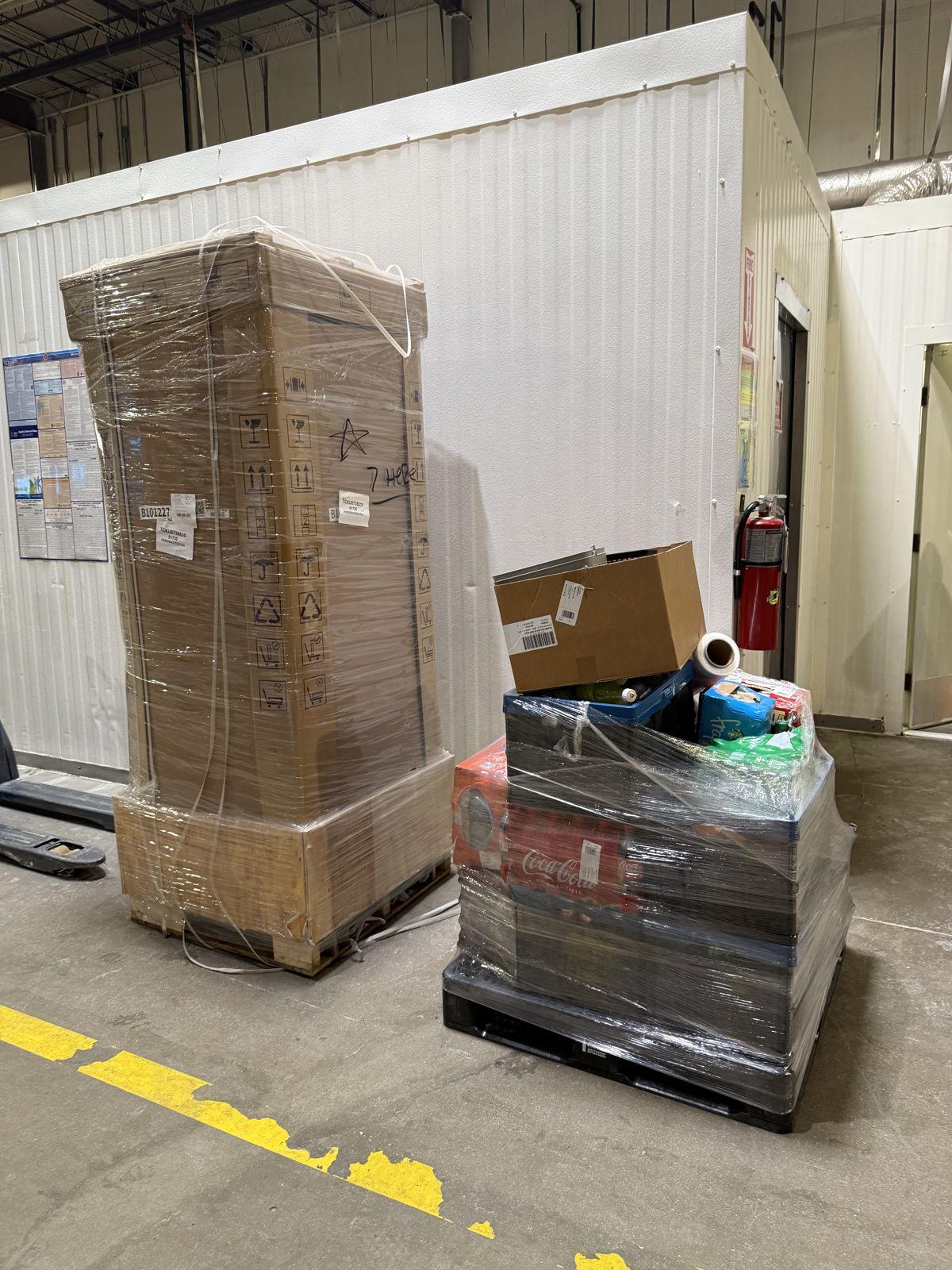 A tall wrapped pallet and a smaller loaded pallet are staged with warehouse moving equipment.