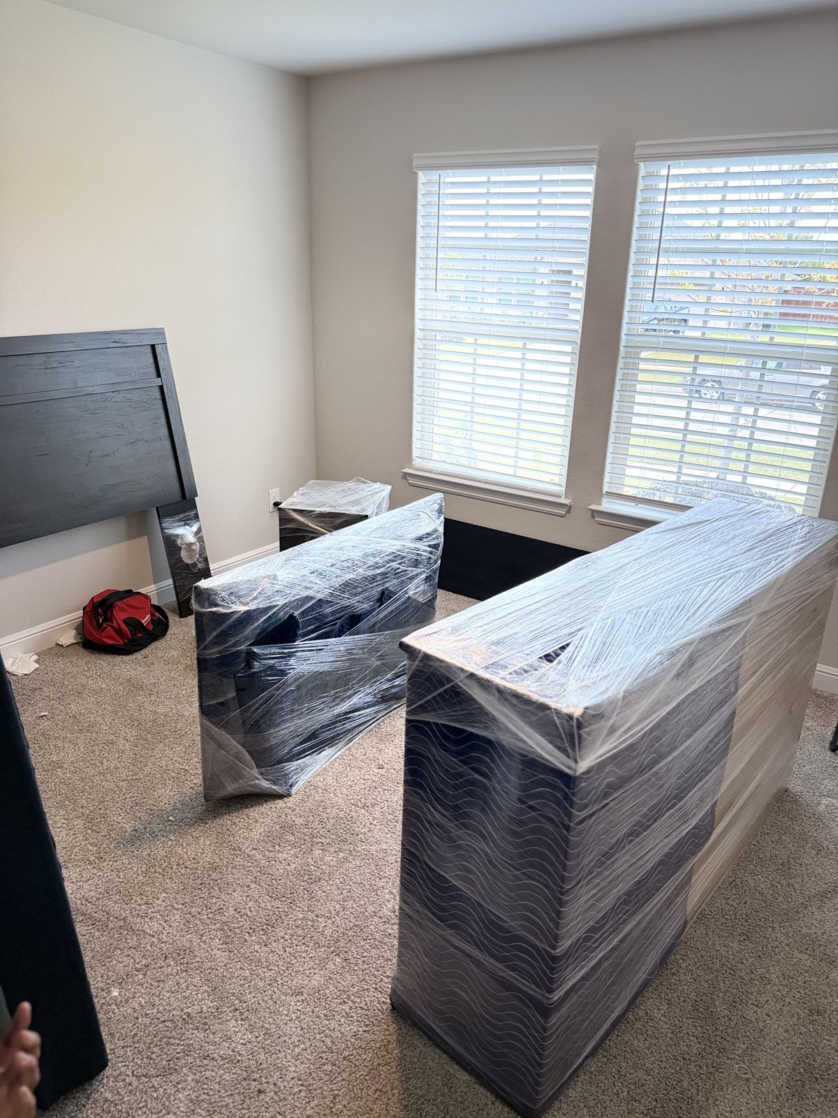 Furniture wrapped in protective blankets and plastic stands ready for transport inside a bright bedroom.