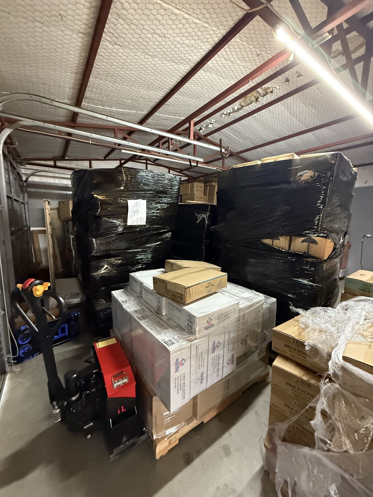 Large black-wrapped loads and boxed products are staged on pallets with moving equipment in a warehouse.