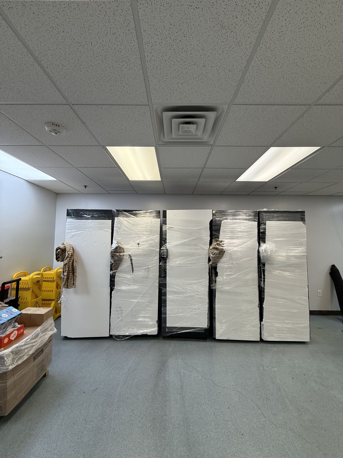 Five large commercial refrigerator units are protected with stretch wrap and padding for relocation.