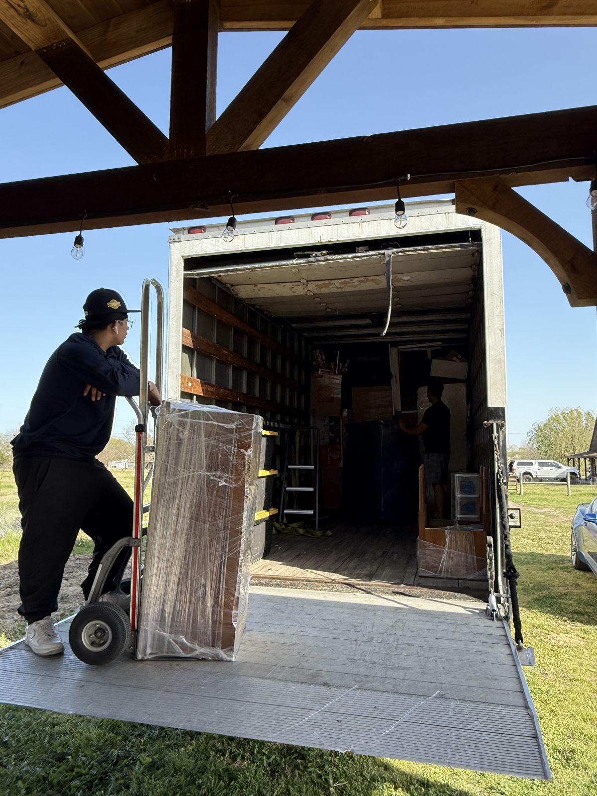 A TL Moving crew member guides wrapped furniture on a hand truck beside an open box truck.