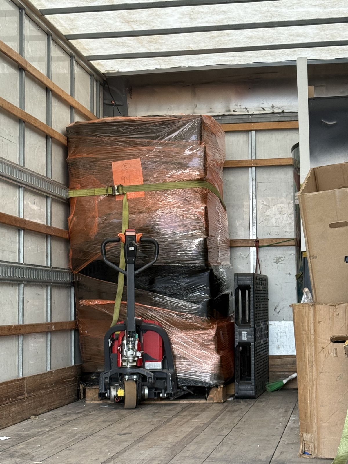 Multiple furniture pieces are wrapped, strapped, and loaded inside a moving truck with powered moving equipment.