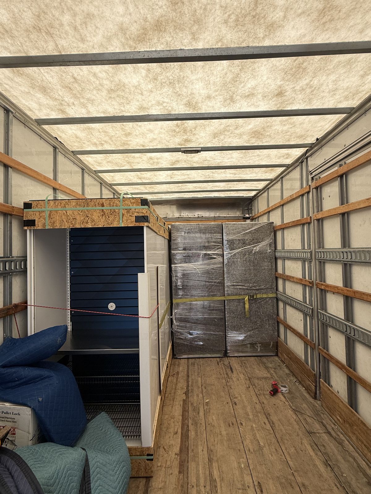 Wrapped cabinets, crated items, and moving blankets are arranged inside a TL Moving truck.
