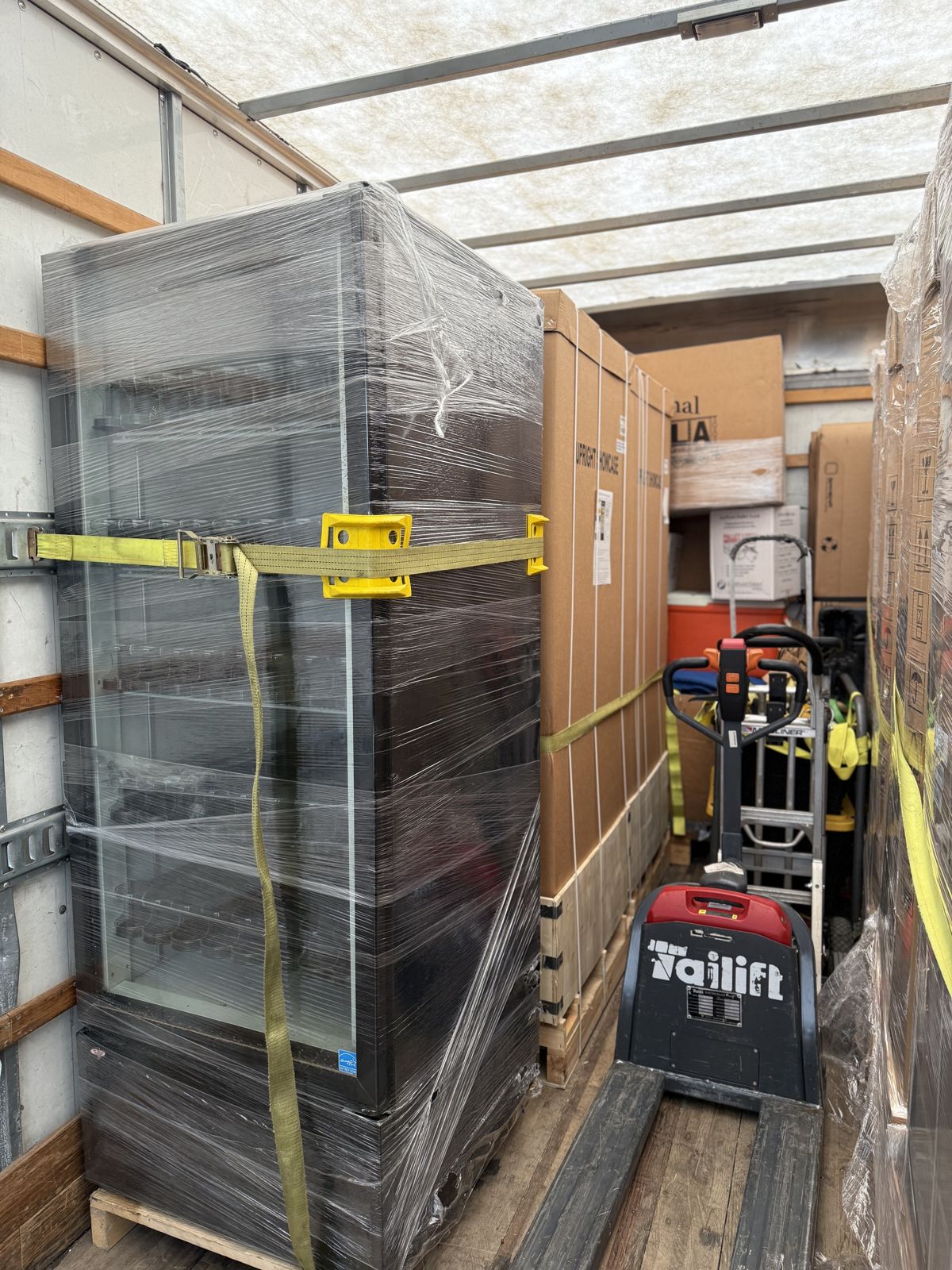 A wrapped vending machine and large cartons are strapped securely inside a moving truck with an electric pallet jack.